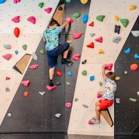 Zwei Kinder klettern an einer bunten Boulderwand mit verschiedenen farbigen Griffen und Tritten. Die Wand bietet abwechslungsreiche Routen und eine spannende Herausforderung in einer sicheren Indoor-Umgebung. Perfekt zum Spielen, Ausprobieren und Fördern motorischer Fähigkeiten.