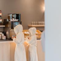 Zwei Kinder in wei&szlig;en Badem&auml;nteln bedienen sich an einer Getr&auml;nkestation im Spa-Bereich. Die freundliche Atmosph&auml;re und das moderne Design sorgen f&uuml;r Wohlf&uuml;hlmomente. Im Hintergrund stehen Gl&auml;ser bereit, w&auml;hrend warme Farben Gem&uuml;tlichkeit ausstrahlen.
