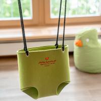 Die hochwertige gr&uuml;ne amiamos Baby-Schaukel aus weichem Filz h&auml;ngt sicher an schwarzen Seilen vor einem sonnendurchfluteten Fenster. Im Hintergrund sorgt ein pl&uuml;schiges gr&uuml;nes Spielkissen f&uuml;r eine gem&uuml;tliche, kinderfreundliche Atmosph&auml;re im Raum. Perfekt f&uuml;r spielerische Indoor-Momente.