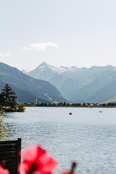 Ein idyllischer Blick über den Zeller See mit leuchtenden Blumen im Vordergrund und imposanten Alpen im Hintergrund. Das klare Wasser lädt zum Entspannen ein, während Boote die ruhige Szenerie beleben. Perfekte Kulisse für Natur- und Outdoorliebhaber.