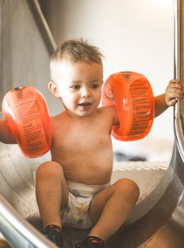 Kleinkind mit Schwimmflügeln beim Rutschen