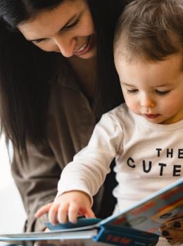 Eine Mutter und ihr Kleinkind genie&szlig;en gemeinsam eine liebevolle Vorlesestunde. Das Kind zeigt neugierig auf ein buntes Bilderbuch, w&auml;hrend die Mutter l&auml;chelnd zusieht. Die Szene vermittelt Geborgenheit, N&auml;he und Freude am gemeinsamen Entdecken von Geschichten.