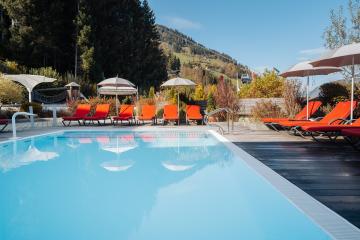 Der beheizte Außenpool mit kristallklarem Wasser lädt zum Entspannen ein. Bequeme, orange Liegen und Sonnenschirme umgeben den Pool, während die malerische Berglandschaft im Hintergrund für ein einzigartiges Urlaubsambiente sorgt. Perfekt für entspannte Stunden im Freien.