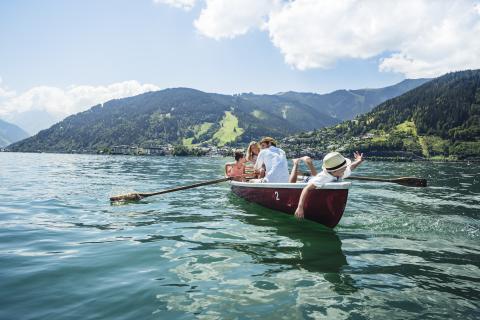 Eine Gruppe genießt eine entspannte Ruderbootfahrt auf einem klaren See, umgeben von beeindruckenden Bergen und grünen Hängen. Das Licht strahlt freundlich auf das Wasser, während die Bootsinsassen gemeinsam die beruhigende Naturkulisse und den weiten Panoramablick erleben.