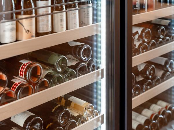 Zahlreiche Weinflaschen liegen ordentlich in einem modernen, beleuchteten Weink&uuml;hlschrank. Die Regale sind aus Holz gefertigt und sorgen f&uuml;r eine stilvolle Pr&auml;sentation der erlesenen Weinauswahl. Die LED-Beleuchtung hebt das Ambiente hervor und garantiert optimale Lagerbedingungen.