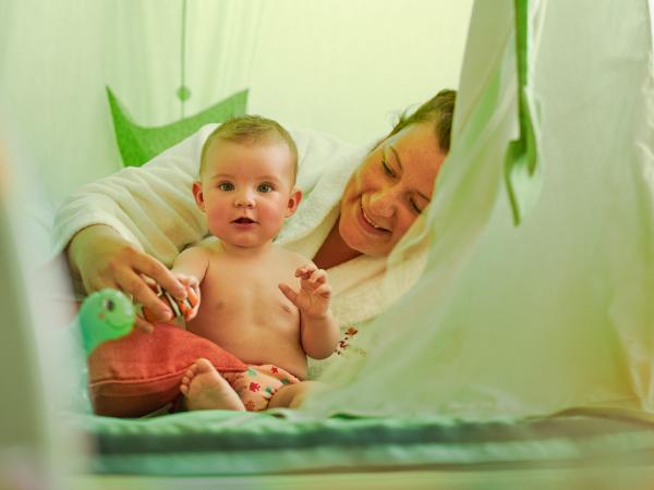 Ein Baby spielt fr&ouml;hlich mit seiner Mutter in einem lichtdurchfluteten, gr&uuml;nen Spielzelt. Die Szene strahlt Geborgenheit und Freude aus, mit weichen Stoffelementen und liebevoller Atmosph&auml;re &ndash; ideal f&uuml;r gemeinsame Entdeckungen und entspannte Momente.