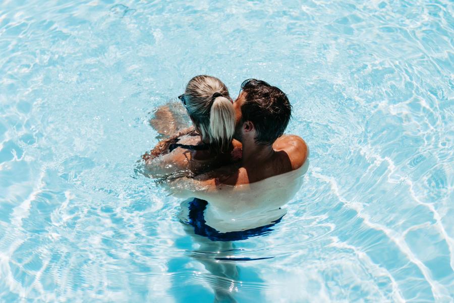 Ein verliebtes Paar umarmt sich liebevoll in einem klaren Au&szlig;enpool bei strahlendem Sonnenschein. Das Wasser schimmert t&uuml;rkisblau, w&auml;hrend Sonnenstrahlen f&uuml;r lebendige Reflexionen sorgen. Die entspannte Atmosph&auml;re l&auml;dt zum Verweilen und Wohlf&uuml;hlen ein &ndash; ideale Kulisse f&uuml;r eine Auszeit zu zweit.